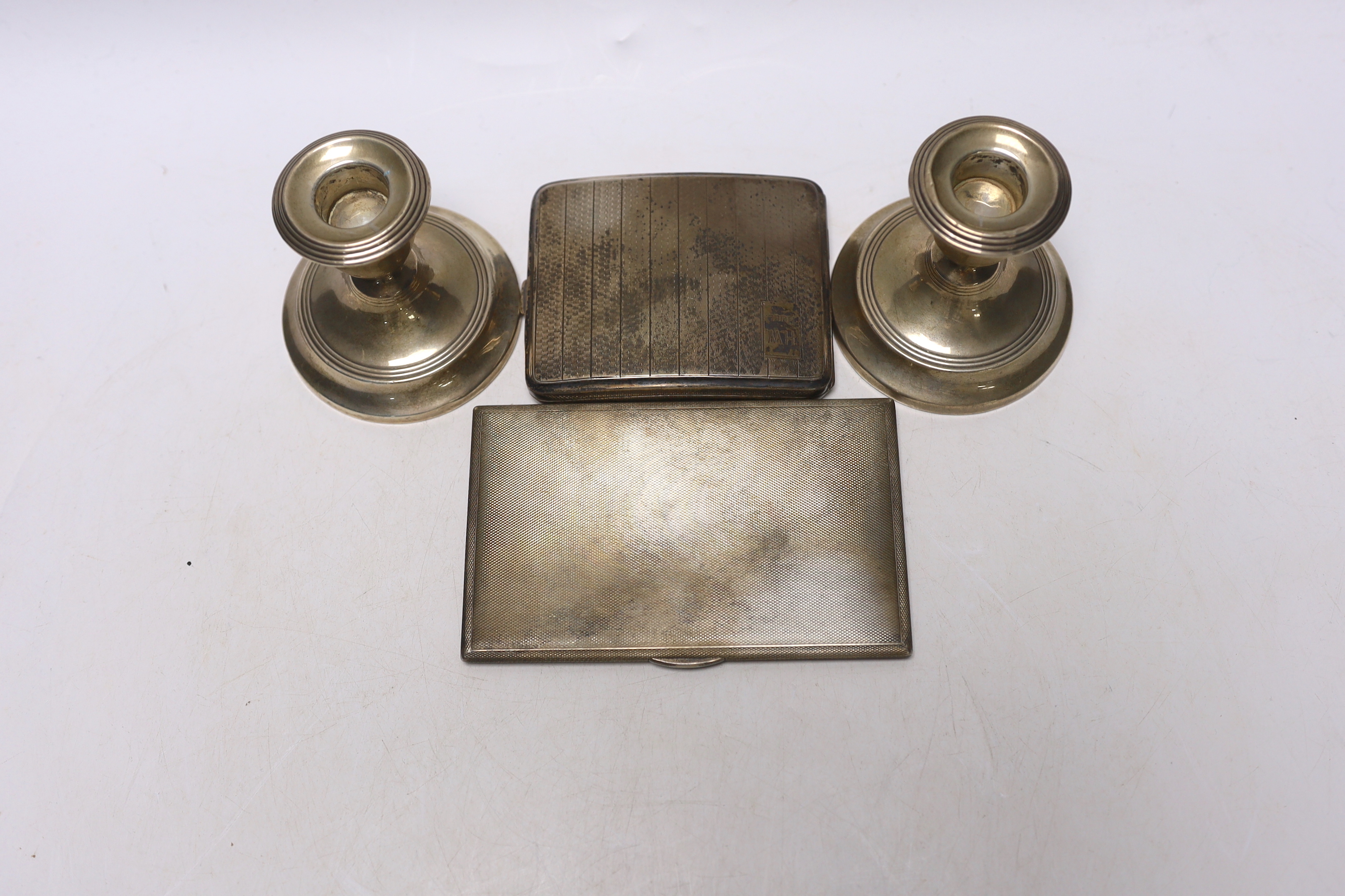 Two engine turned silver cigarette cases, largest 13.5cm and a pair of silver mounted dwarf candlesticks.